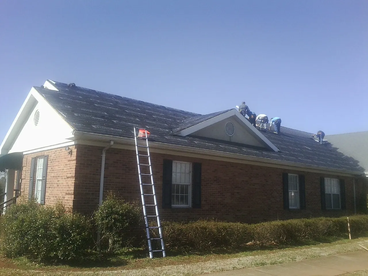 Crew tearing shingles off a brick ranch roof with a ladder set — Emergency Roof Repair work by our crew in Southborough