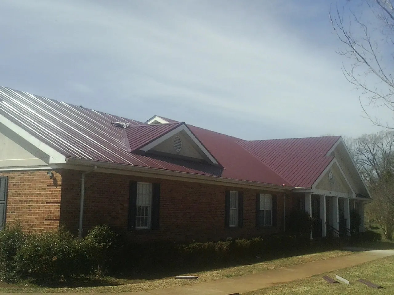 Red metal roof with gabled entries on a long brick building, from a Hail Damage Roof Repair job in Southborough