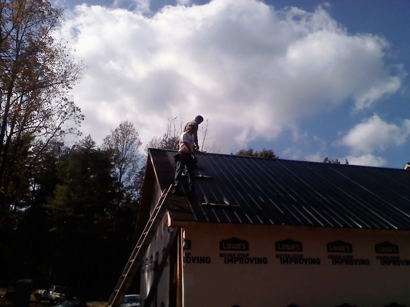 Roofer fastening dark metal panels high against a cloudy sky, from a Roof Inspection job in Southborough