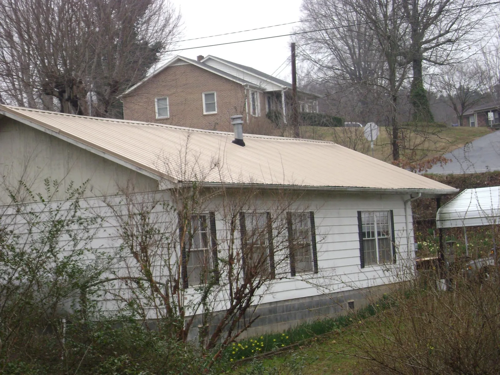 Tan metal roof on a white sided house set into a hillside — Commercial Roofing by Roofing Brothers in Southborough